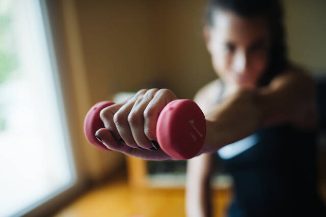 Girl doing exercises at home. Holding weight closeup.