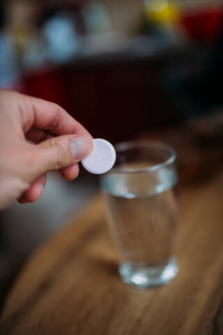 Man holding an effervescent tablet above the glass of water.