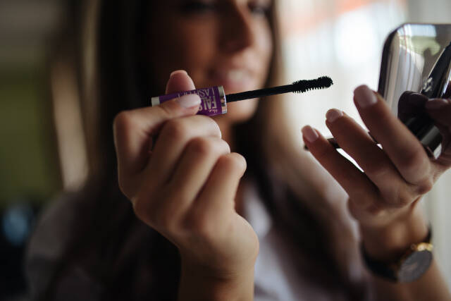 Woman applying mascara to her eyelashes.