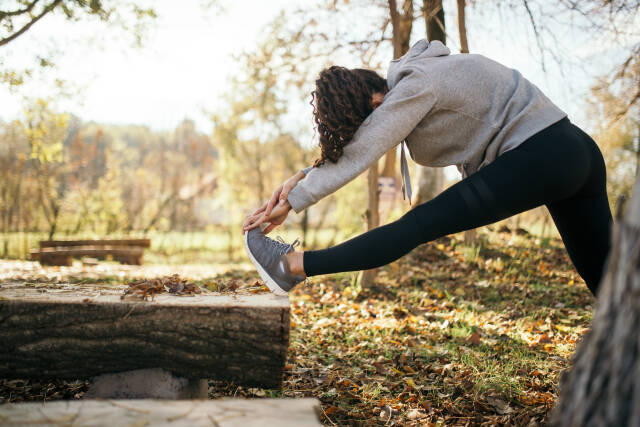 Woman stretching her hamstrings and glutes on a log in nature.