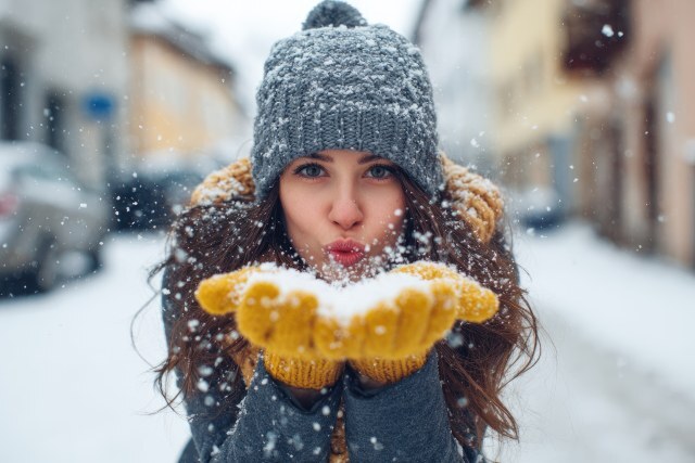 Glückliche Frau pustet Schnee aus ihre gelben Handschuhe