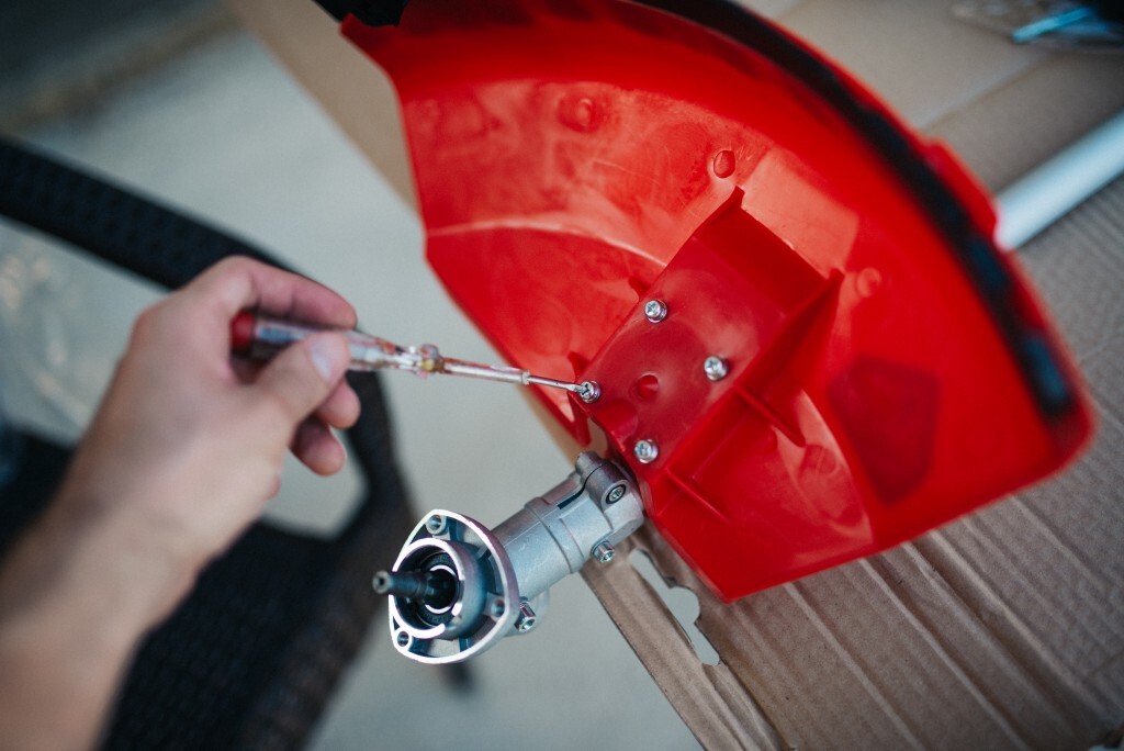 A man focuses on fixing his red grass trimmer