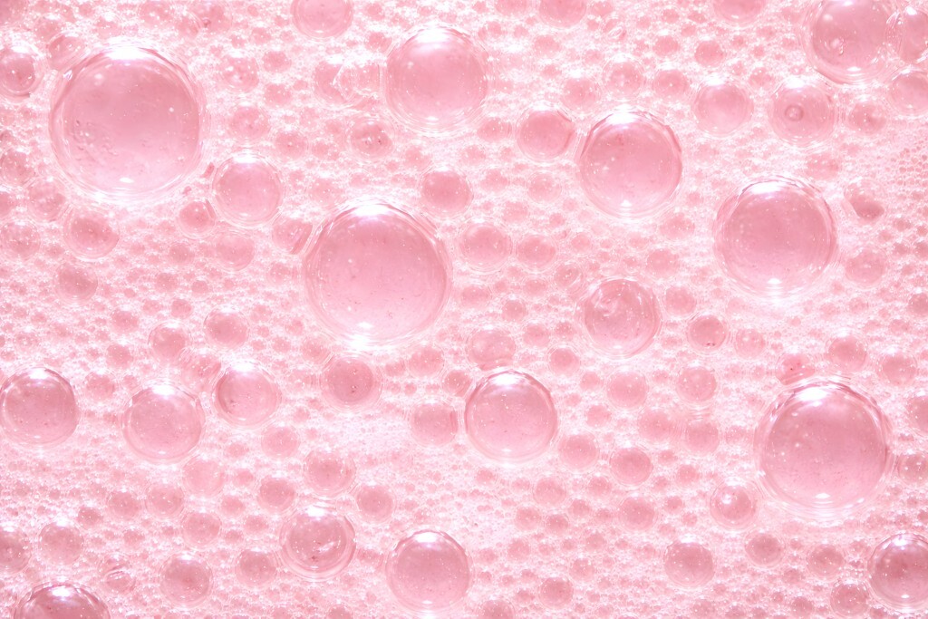 Zartrosa Seifenblasen auf schaumiger Wasseroberfläche
