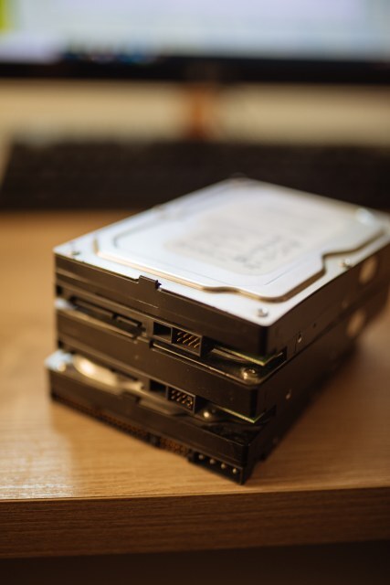 Three old hard drives are carefully positioned on top of each other on a wooden surface