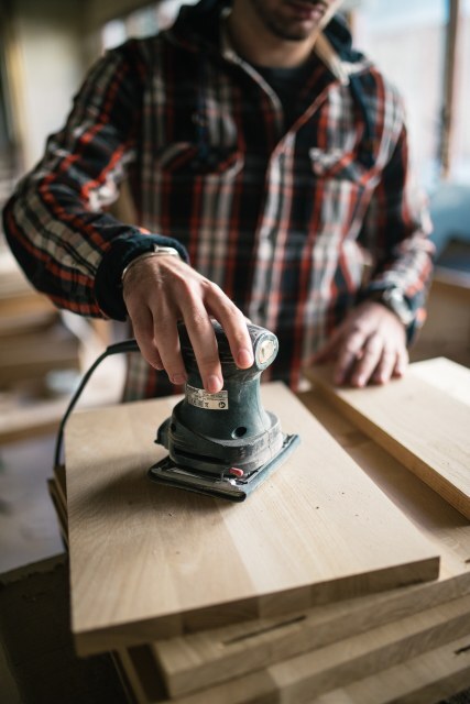 Carpenter using electric sander to smooth wooden boards