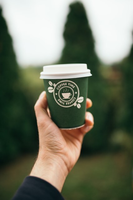 A person holds a green coffee cup with a logo