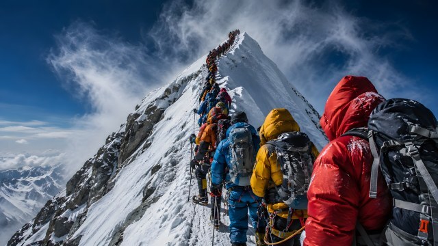 Bergsteiger in langer Schlange auf verschneitem Gipfelgrat