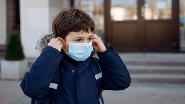 Schulkind setzt Atemschutzmaske vor Schulgebäude auf